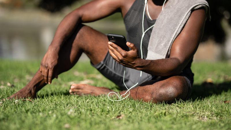 Someone in training gear sitting on the grass with a phone